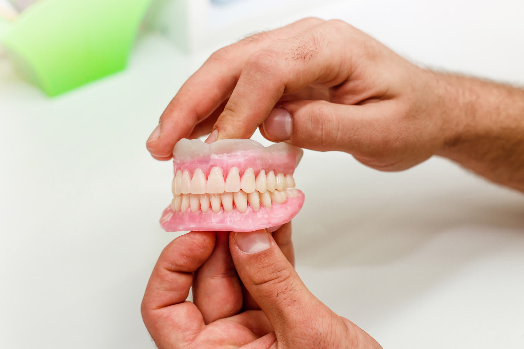 A person holding a set of full upper and lower dentures with both hands in a dental office.