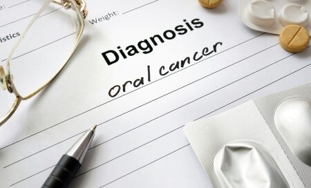 A medical diagnosis form with the words "oral cancer" written on it, accompanied by a pen, eyeglasses, and medication tablets.