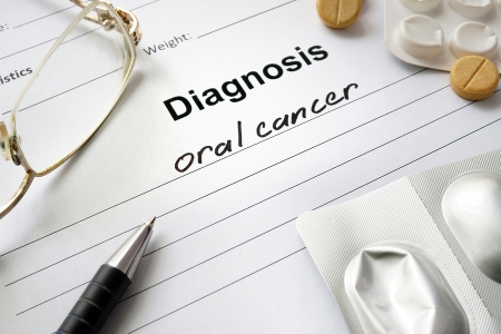 A medical diagnosis form with the words "oral cancer" written on it, accompanied by a pen, eyeglasses, and medication tablets.