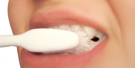 Close-up of a person brushing their teeth with a white toothbrush, showing the white bristles in contact with their teeth.