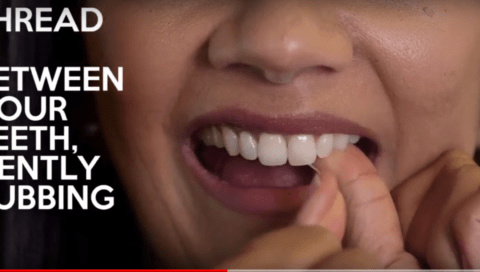 A person demonstrates how to floss their teeth, with text on the image saying "THREAD BETWEEN YOUR TEETH, GENTLY RUBBING.