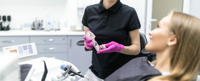 Closeup of dentist's hands explaining teeth model to female patient at clinic