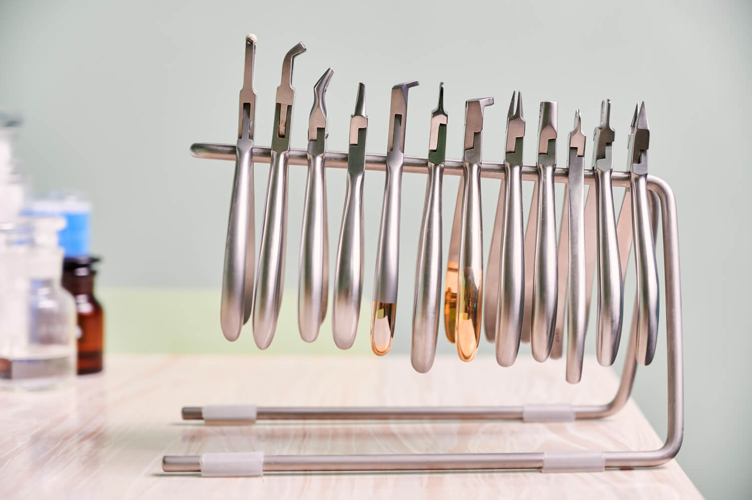 A set of metal dental instruments, including various pliers and forceps, organized in a steel rack on a light wooden table, showcases the precision tools essential for exceptional dental services.