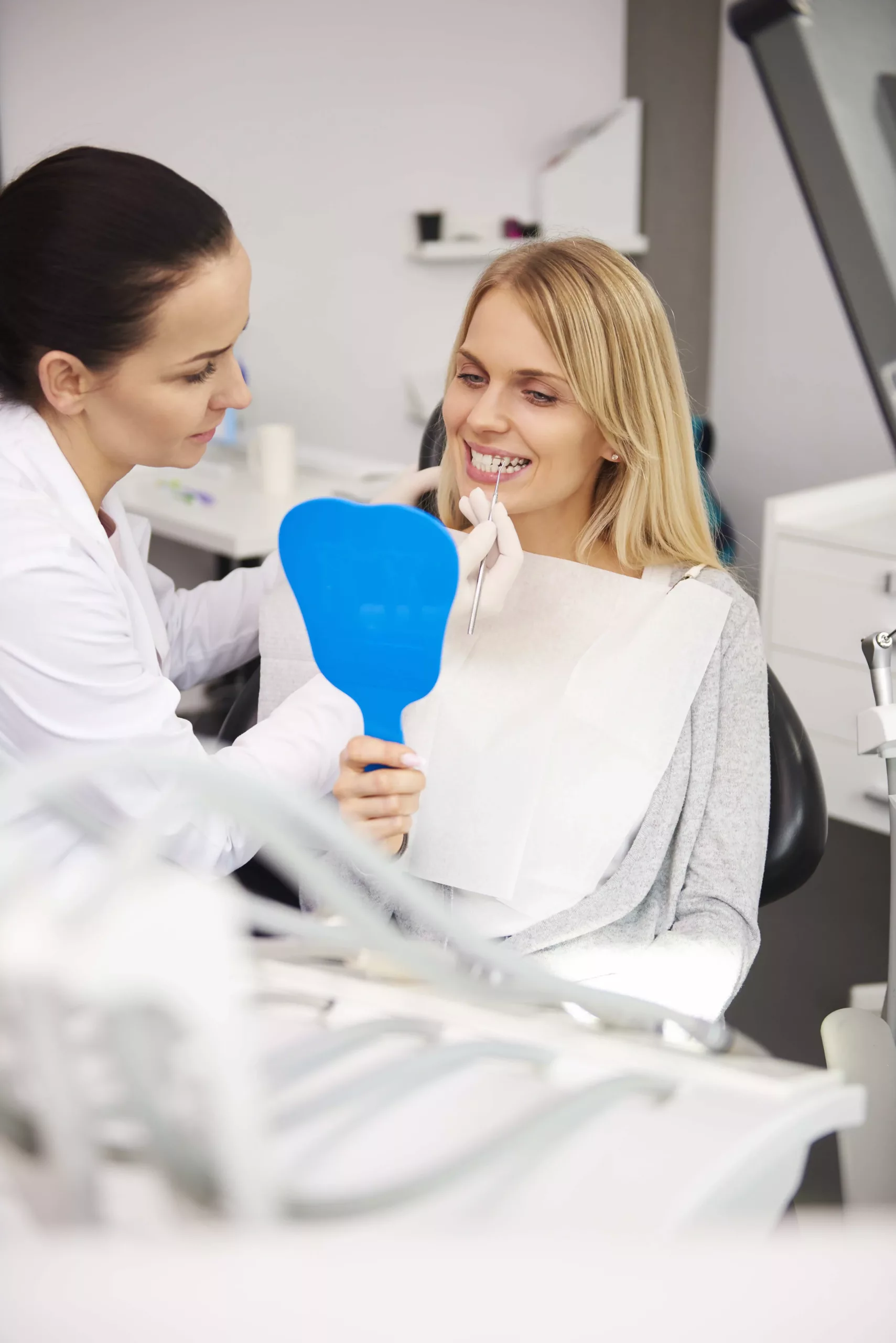 female-dentist-examining-woman A dentist showing a female patient her teeth using a blue hand mirror during a dental check-up.
