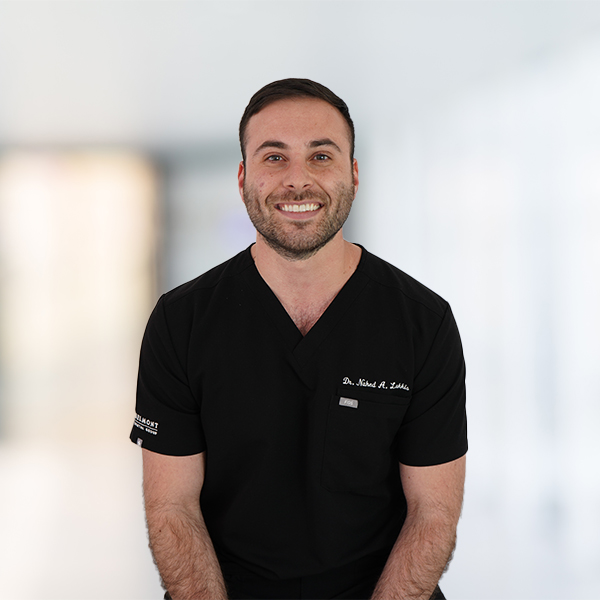 Nahed Lakkis, DMD, dressed in a black medical uniform, smiles at the camera. The background is blurred, suggesting an indoor setting.