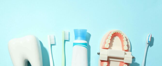 A toothbrush, toothpaste, dental model, and oversized tooth are arranged on a light blue background.