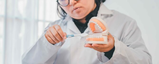A person in a lab coat demonstrates brushing teeth using a toothbrush and a dental model, highlighting the benefits of dental irrigation for maintaining oral health.